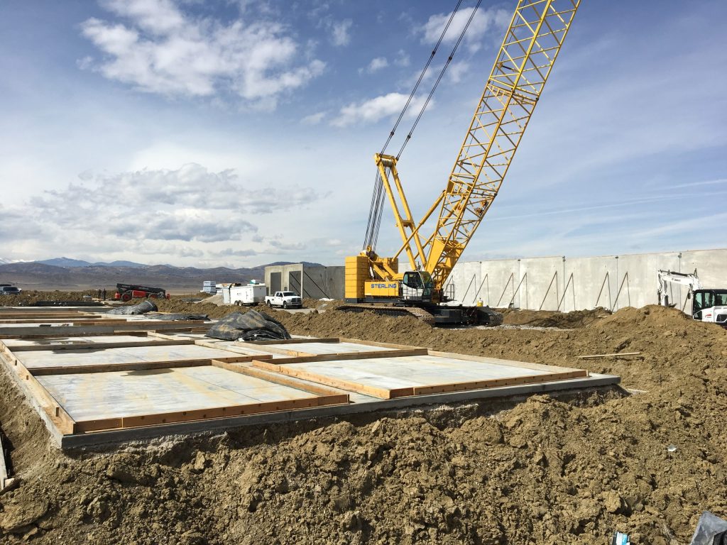 new homes in windsor co are prepared as we see here with graded site work, foundations, and heavy equipment. we see mountains in the background. a congrete slab. and a crane.